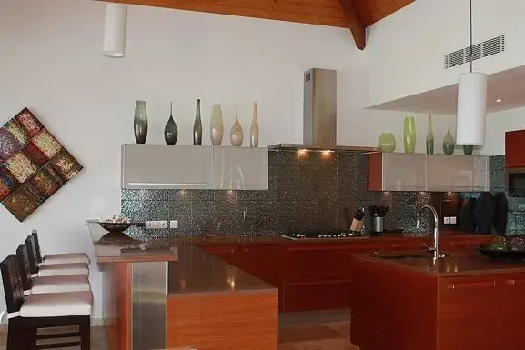 The modern kitchen showcases dark wood cabinetry, an island with sink, breakfast bar with four stools, and decorative vases adorning the cabinet tops.