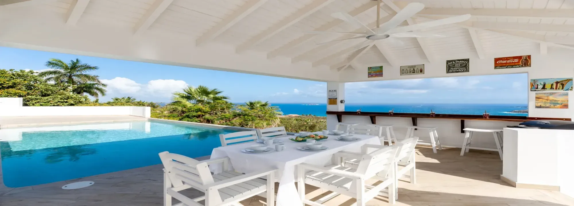 Luxury villa terrace with a white dining set and an infinity pool overlooking the tropical ocean landscape