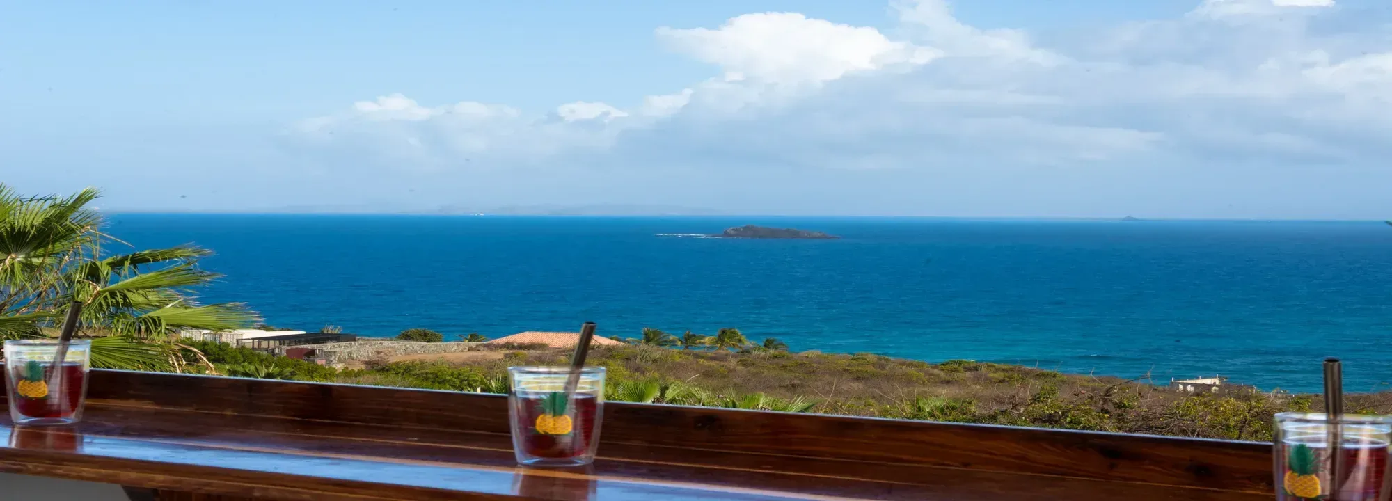 Polished wooden bar with three refreshing cocktails overlooking a stunning panoramic view of the deep blue Caribbean ocean