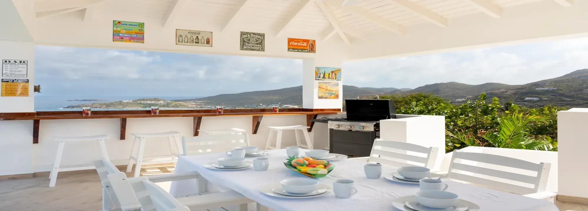 Bright white outdoor terrace featuring a set dining table, outdoor kitchen, and panoramic views of the coastline and mountains