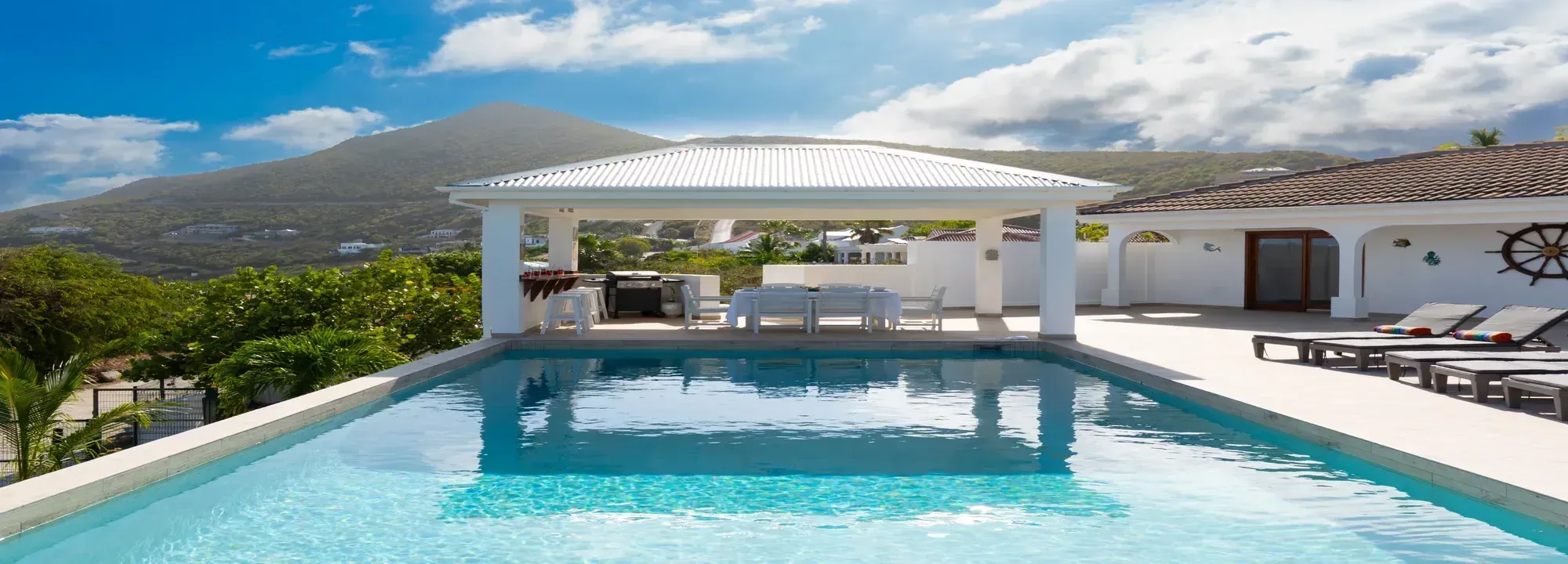 Villa featuring a turquoise swimming pool, a white outdoor dining gazebo, and sun loungers with a mountain backdrop