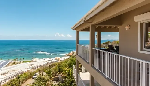 Wake up to panoramic ocean views from this upper-level balcony, where comfortable outdoor seating invites you to linger over morning coffee. White railings frame vistas of Dawn Beach and the shimmering Caribbean, with palm trees and coastal St. Maarten stretching to the horizon.                                                                                                                                                                                                                                     +
 