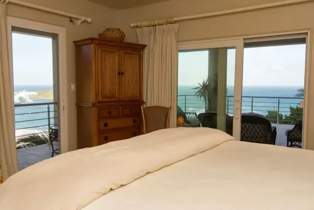 Rest and recharge in this comfortable bedroom with a large bed, wooden armoire, and two upholstered chairs positioned to enjoy the ocean view through sliding doors. Natural textures and wicker accents create a calm Caribbean retreat.                                                                                                                                                                                                                                                                                    +
 