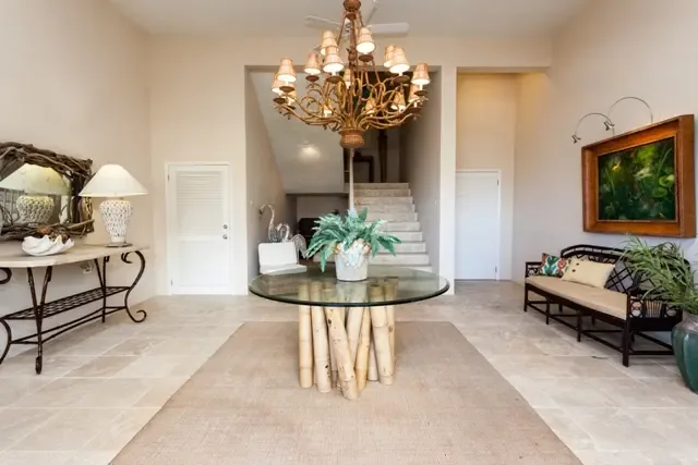 Make a grand entrance in this elegant foyer, where a round glass-top table with artistic wooden base sits beneath an ornate chandelier. High ceilings, a decorative staircase, and a console table with mirror set the tone for Villa Bougainvillea's sophisticated Caribbean style.                                                                                                                                                                                                                                       +
 