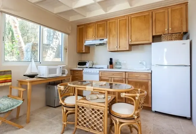 A convenient secondary kitchen with white appliances and a cozy dining nook featuring a round glass table with four wicker chairs. Perfect for casual breakfasts, with greenery views through the window adding a touch of St. Maarten's natural beauty.                                                                                                                                                                                                                                                               +
 