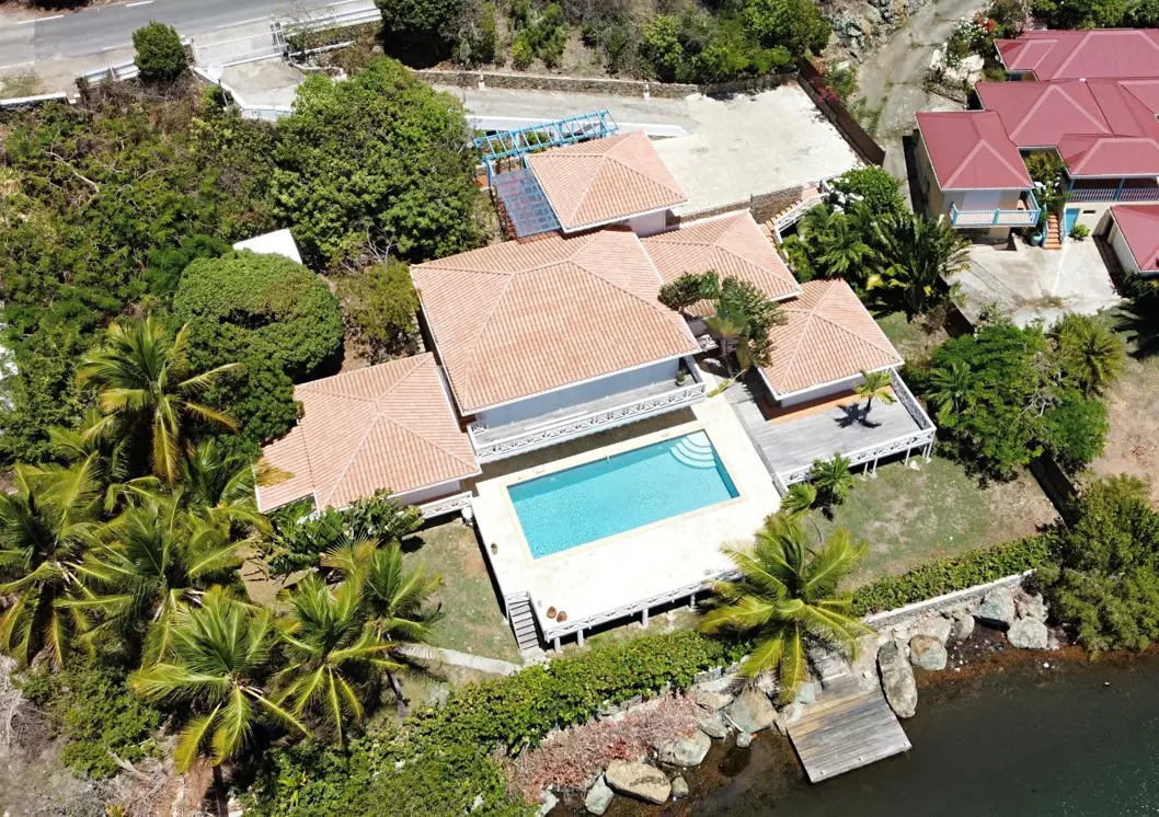Aerial view of Villa Coralita, its private pool, waterfront setting, and boat dock in Oyster Pond.
