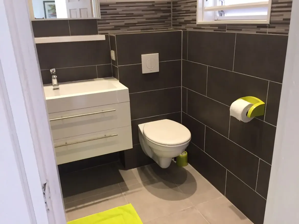 Modern powder room with wall-mounted toilet — dark gray tiles and lime green accents add contemporary style.