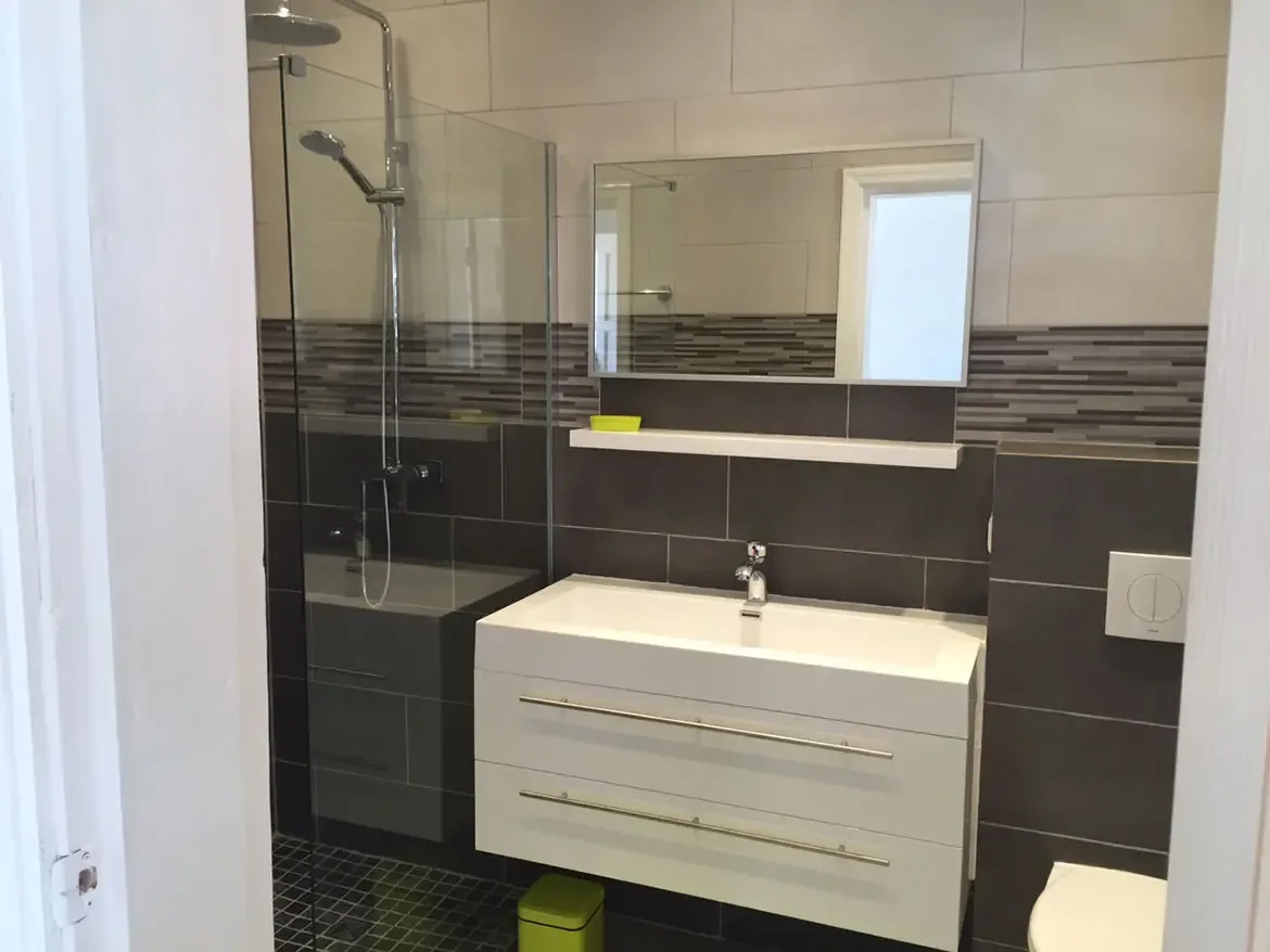 Bathroom with floating vanity and glass shower — gray and cream tiles create a spa-inspired retreat.