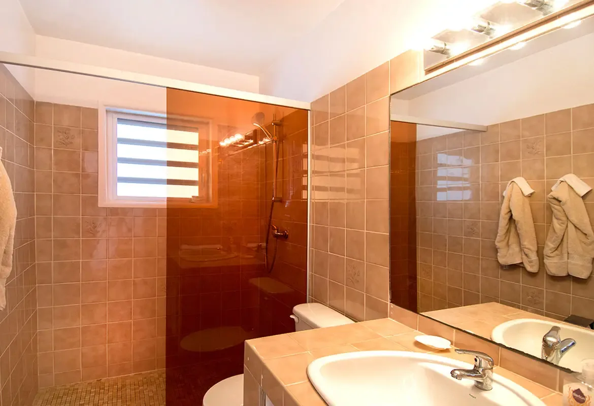 Bathroom with orange glass shower partition — terracotta tiles and natural light create a warm spa feel.