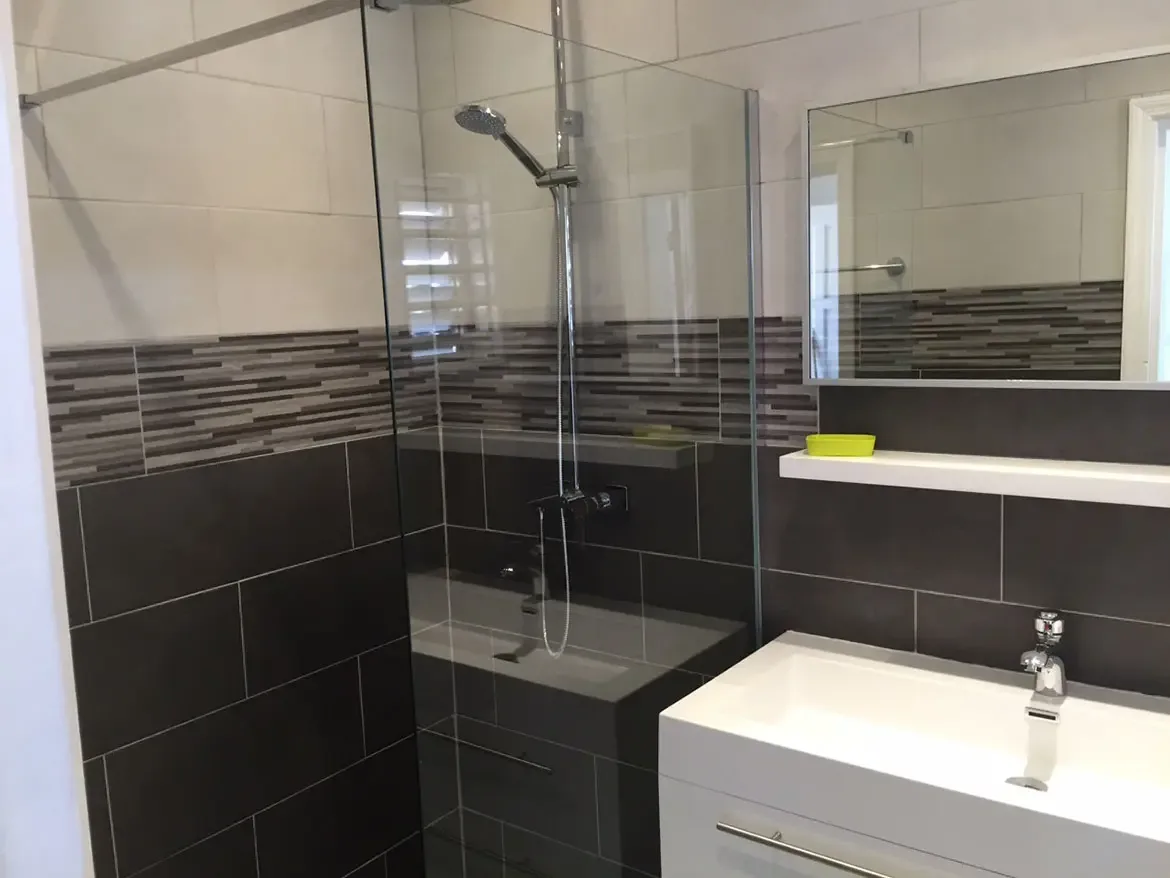 Walk-in shower with two-tone tile and chrome fixtures — the large mirror reflects clean modern design.