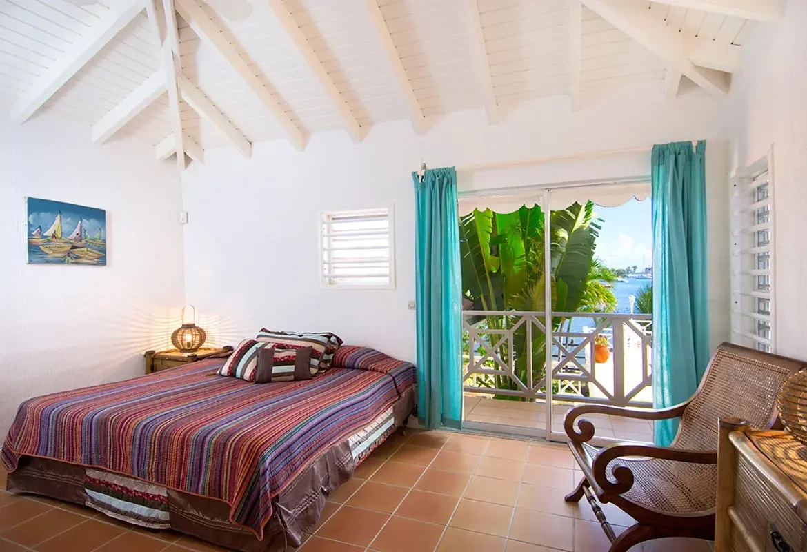 Bedroom with striped bedspread and sailboat painting — sliding doors open to a balcony with tropical views.