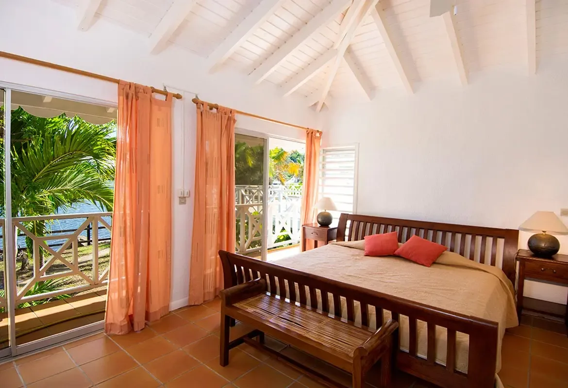 Bedroom with orange curtains and balcony access — the tropical greenery and water views await outside.