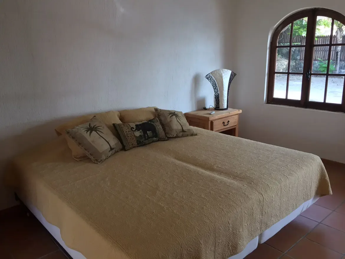 Bedroom with arched window and unique lamp — the tan bedspread and tropical pillows create peaceful elegance.