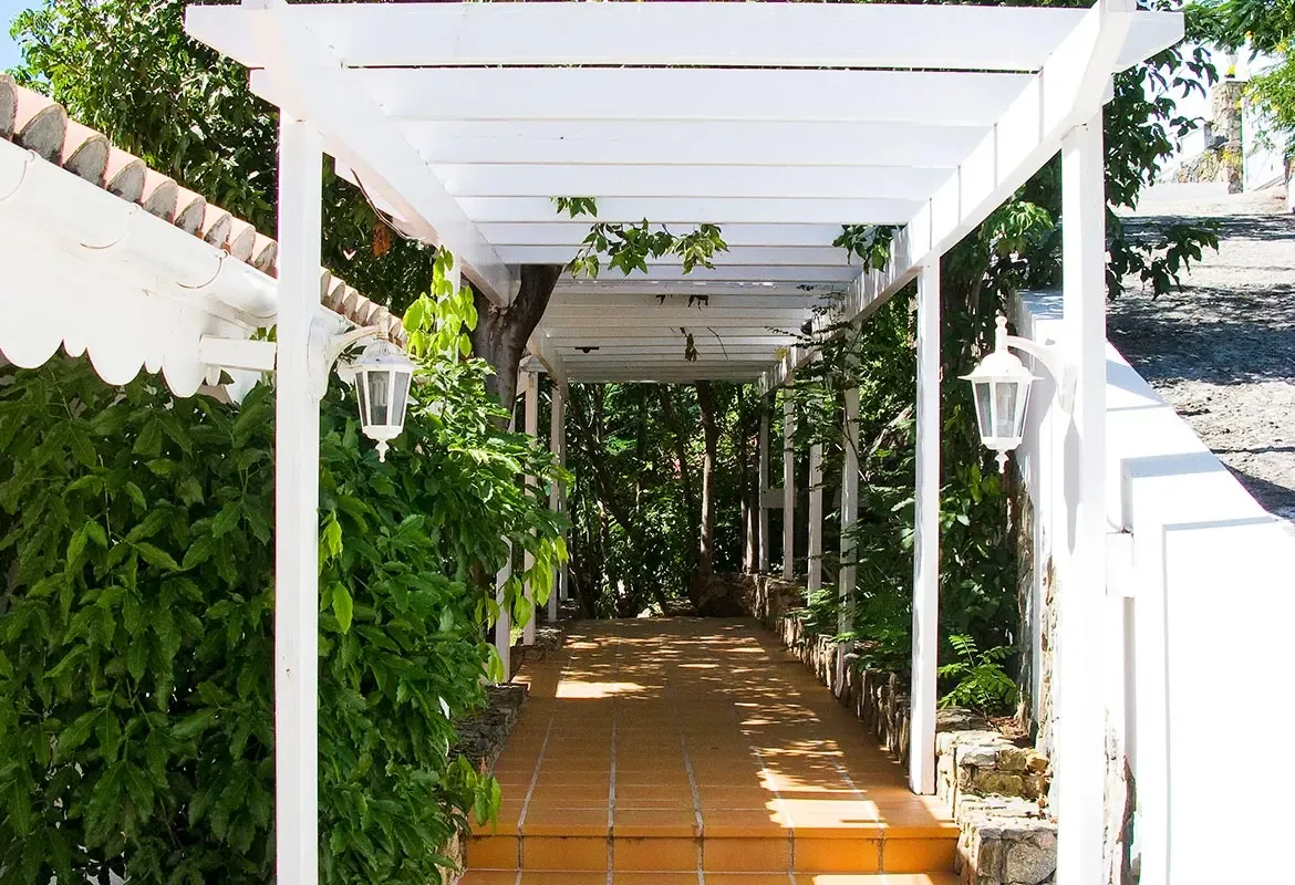 Enter through the white pergola walkway — terracotta tiles and white lanterns welcome you to Caribbean elegance.