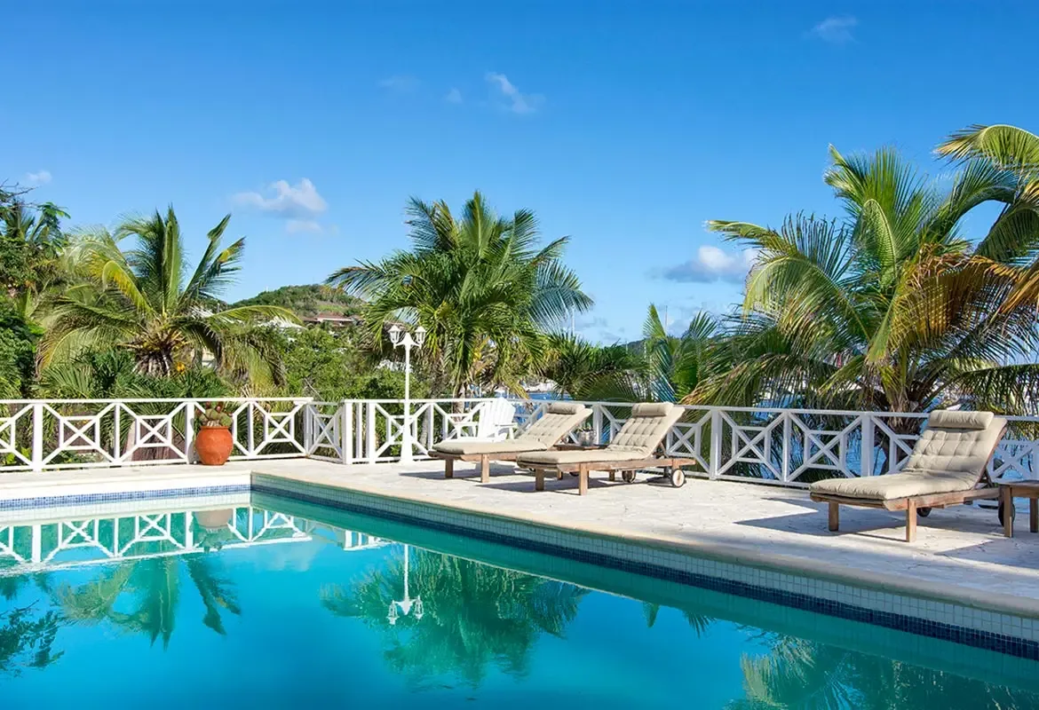 Poolside lounge with white decorative fence — palm trees provide shade for your afternoon swim under blue sky.