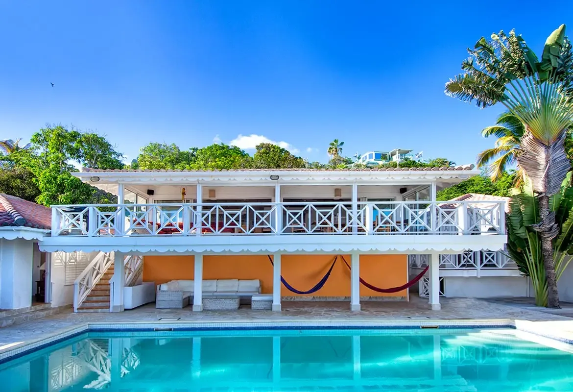 Your private pool with turquoise water and Caribbean architecture — outdoor lounge with hammocks awaits under the orange accent wall.