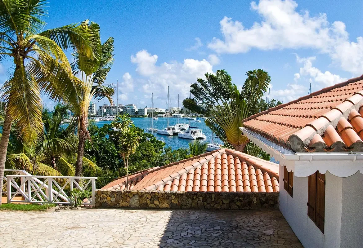 Red-tiled rooftops and stone patio overlook the harbor — white sailboats dot the blue bay below.