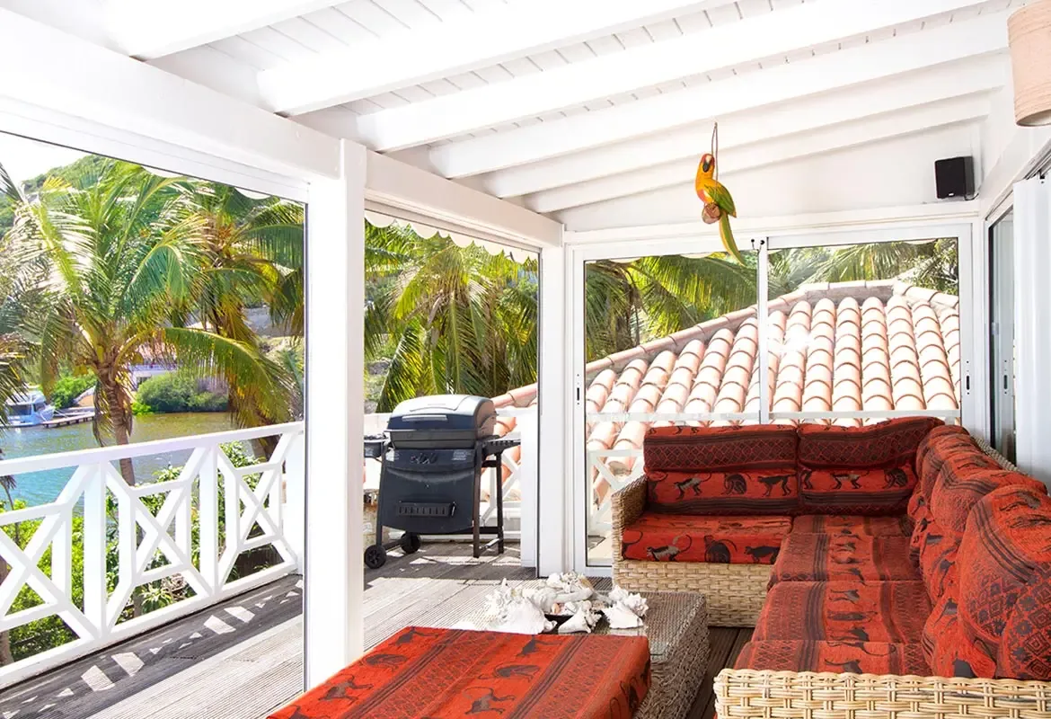 Covered outdoor terrace with wicker sectional and gas grill — water views frame your private BBQ area.