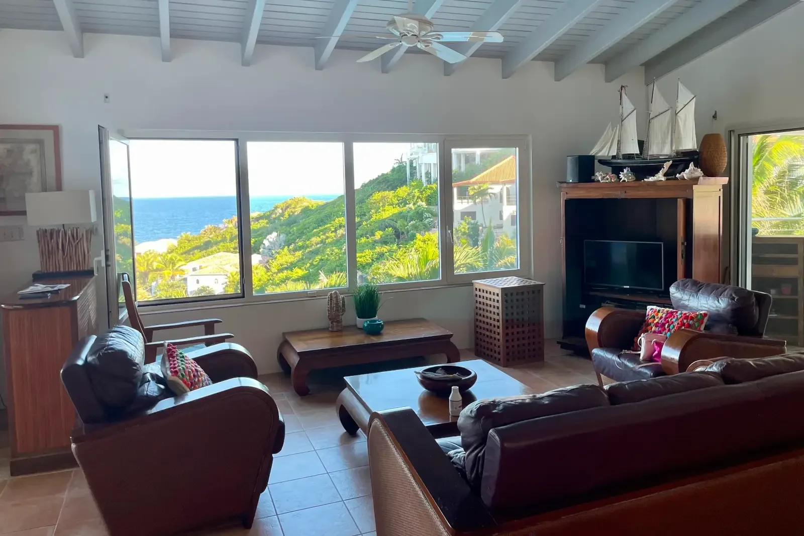 Leather sofas face the ocean through sliding glass doors — relax where indoors meets paradise.