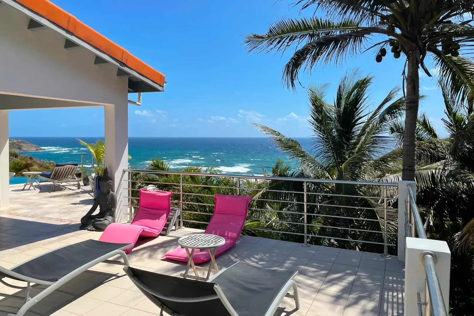 Your private terrace with pink lounge chairs frames the Caribbean — morning coffee with endless ocean views.