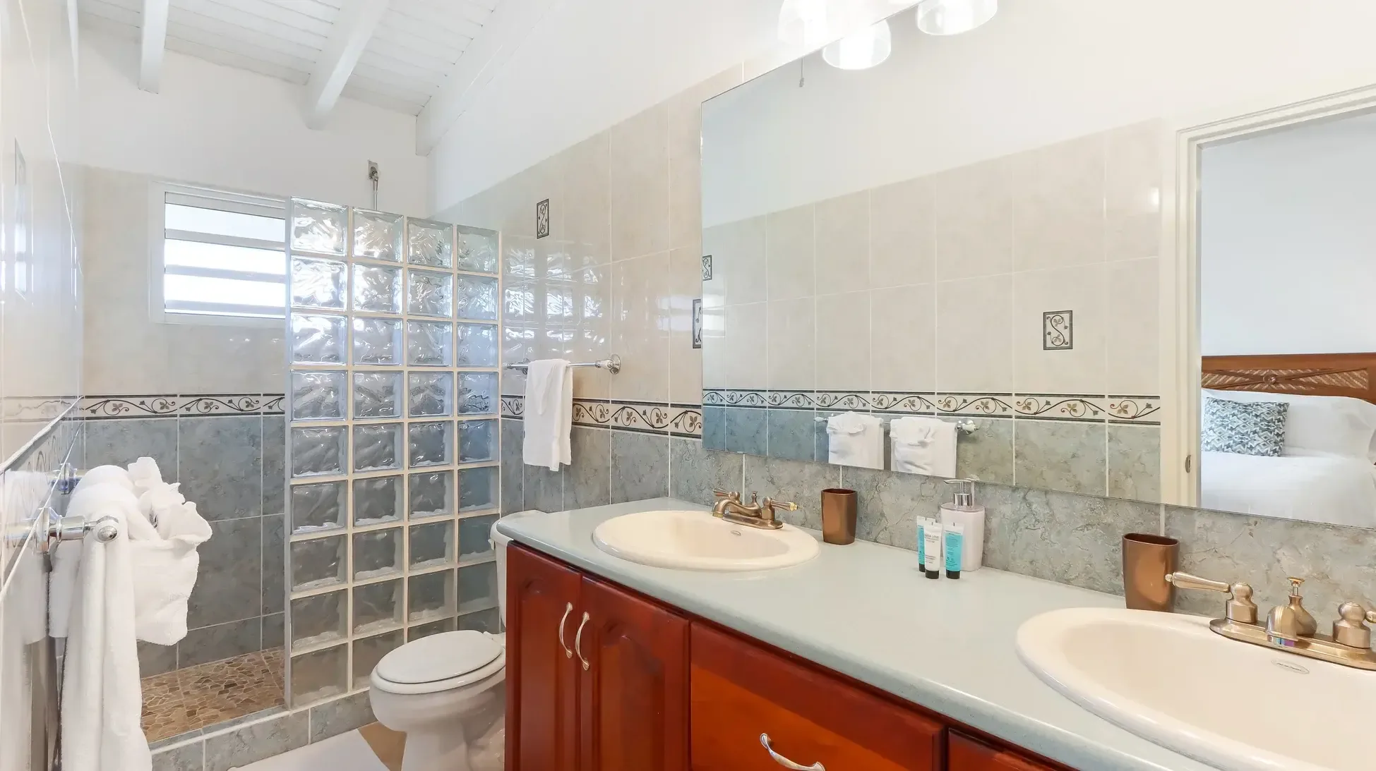 A spa-style double vanity with wood cabinets, dual sinks, and glass block shower wall. Plush white towels and decorative tile complete the retreat.