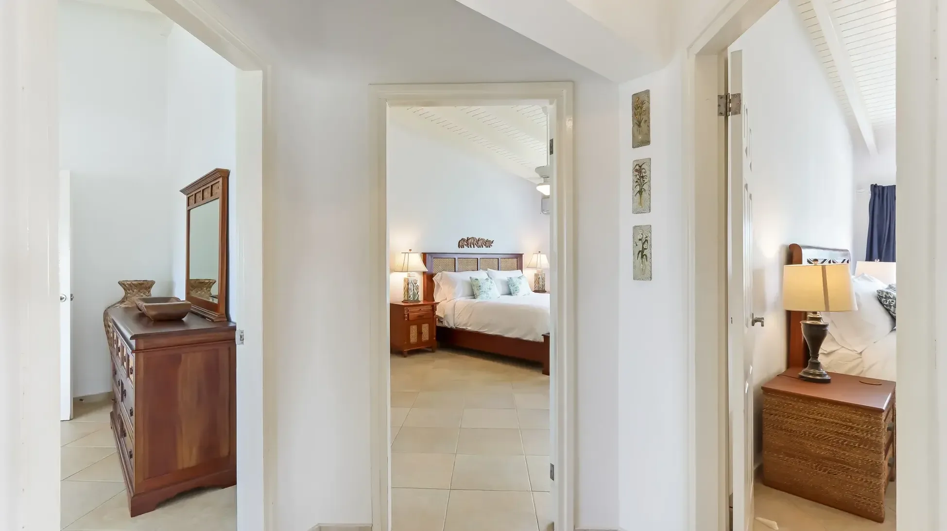 The hallway leading to three bedrooms features a wooden dresser with mirror, vaulted ceilings, and warm lighting.
