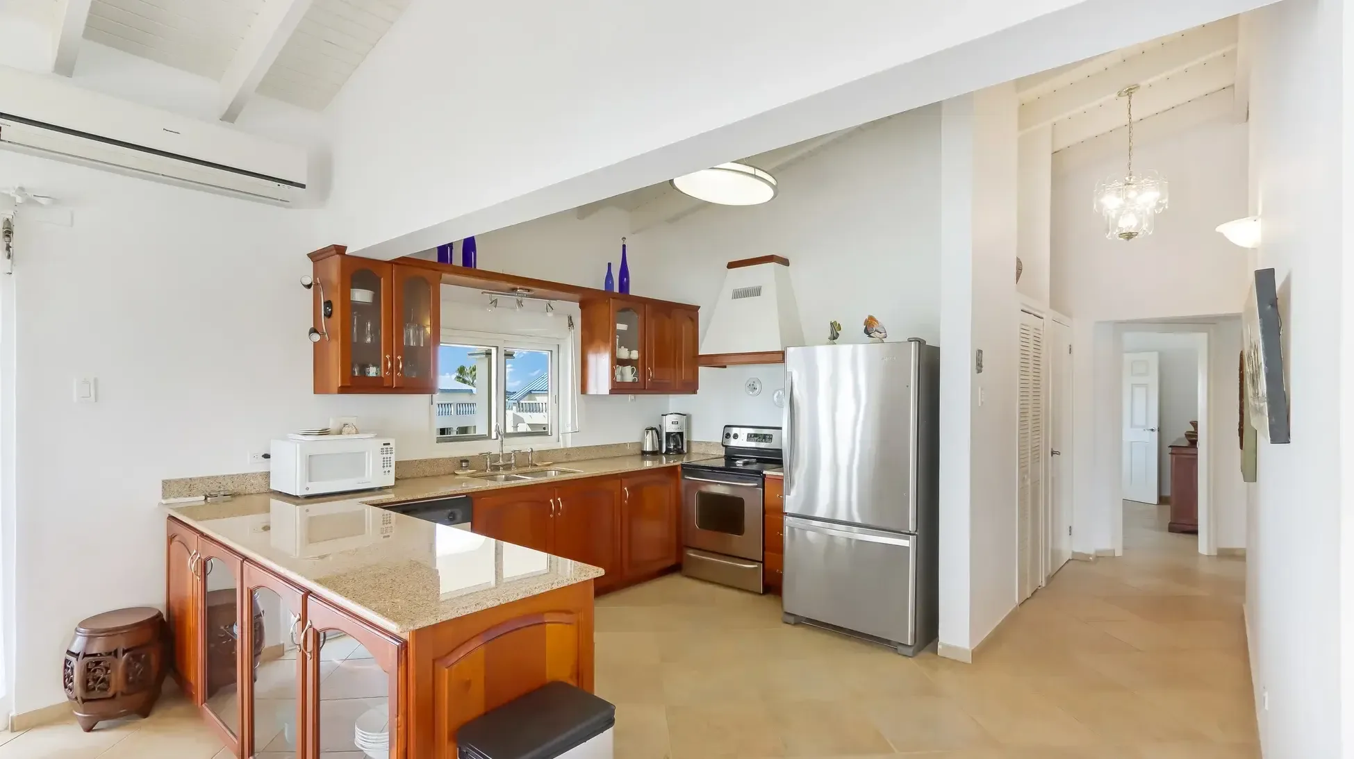 A modern kitchen featuring wood cabinets, granite island, and stainless steel appliances. The window above the sink offers garden views.