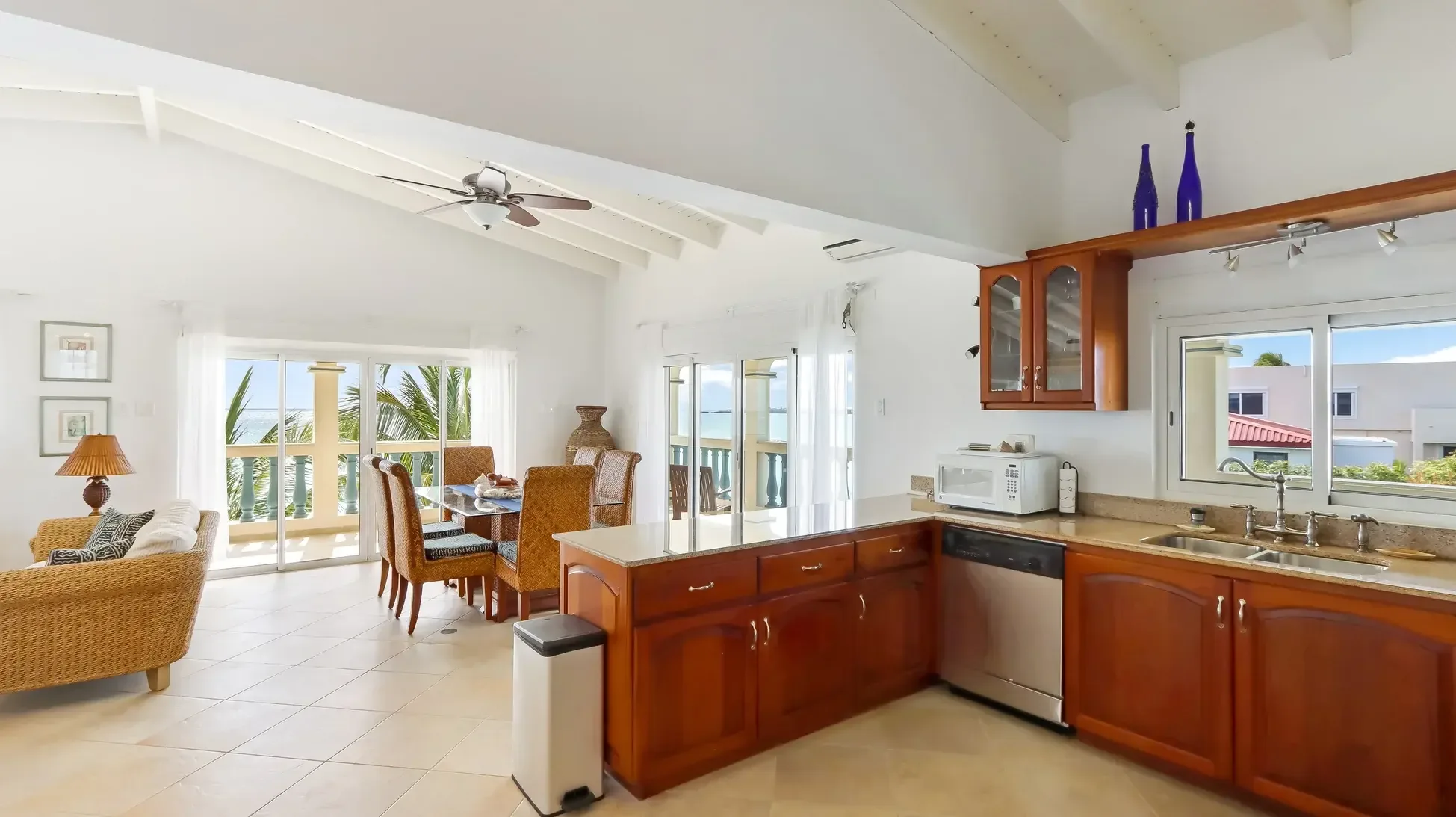 An open kitchen with wood cabinets and granite counters flows into the dining area. Sliding doors reveal the ocean beyond.