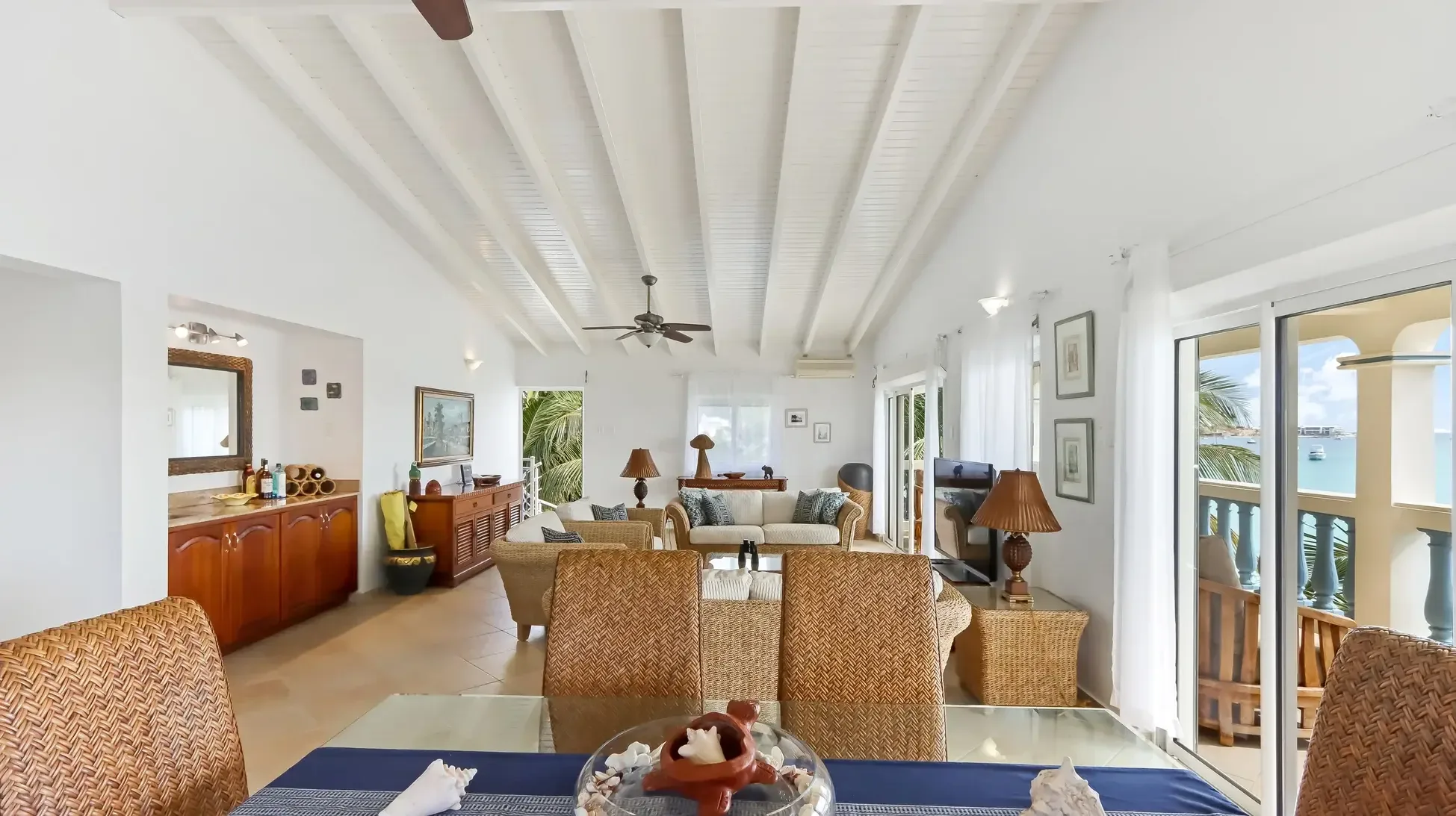 An open living area with wet bar, wicker furniture, and glass dining table. Vaulted ceilings and sliding doors reveal your ocean view.