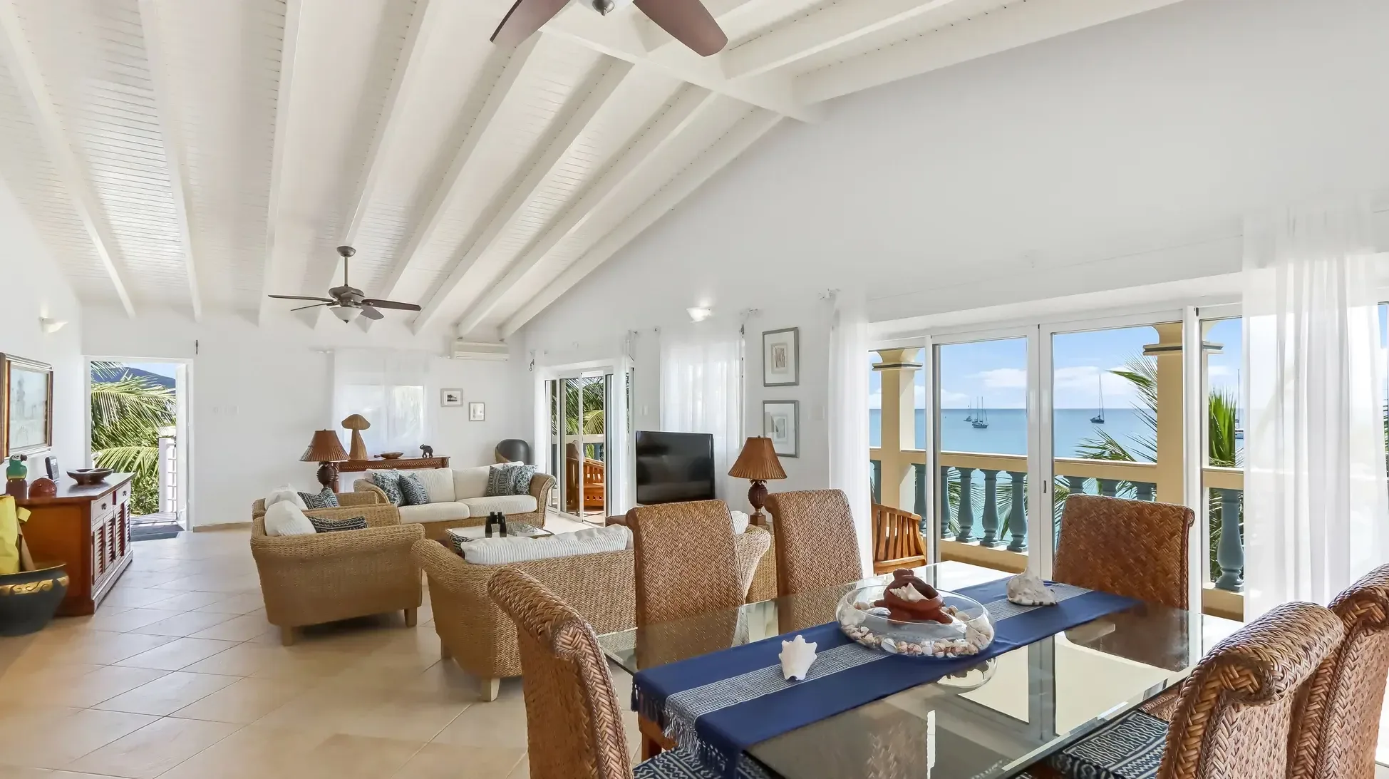 Vaulted ceilings crown this open living and dining space where wicker furniture and glass tables invite you to gaze at panoramic ocean views dotted with sailboats.