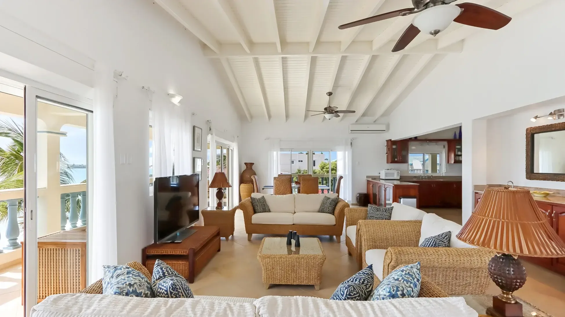Relax in this inviting living space with wicker sofas, blue patterned pillows, and ceiling fans circulating the Caribbean breeze. Sliding doors reveal endless ocean views.