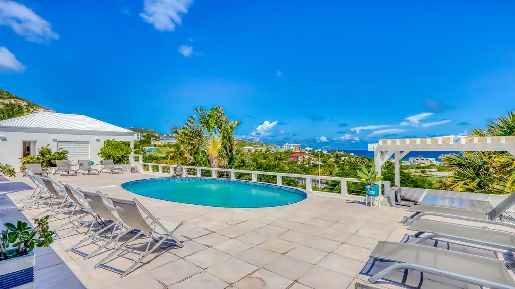 Pool deck with oval pool, loungers, and sea view