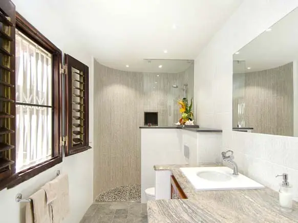 Fresh flowers, pebble-tiled shower floor, and warm Caribbean light through wooden shutters.