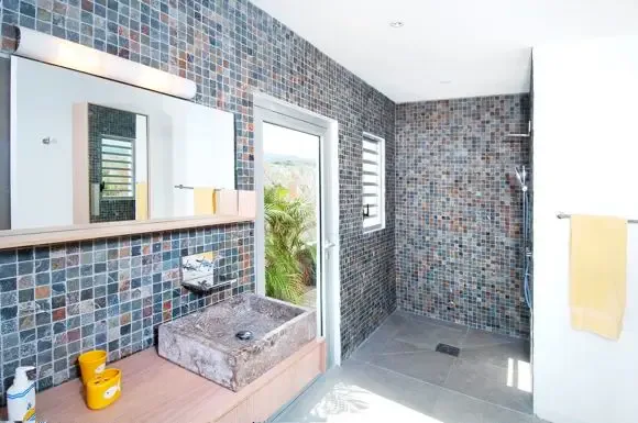 Colorful mosaic tile walls surround a stone vessel sink and wooden vanity, with a walk-in shower area and natural light from adjacent glass doors.                                                                                                                                                                                                                                                                                                                                                                           +
 