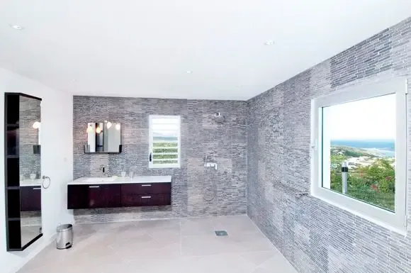 Dark wood vanity and stone-textured tile walls define this modern bathroom, with a walk-in shower and large window offering scenic ocean views.                                                                                                                                                                                                                                                                                                                                                                              +
 