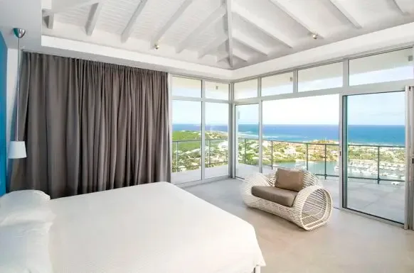 The master suite features a vaulted white-beam ceiling, floor-to-ceiling glass doors opening to a private terrace with sweeping marina and ocean views.                                                                                                                                                                                                                                                                                                                                                                  +
 