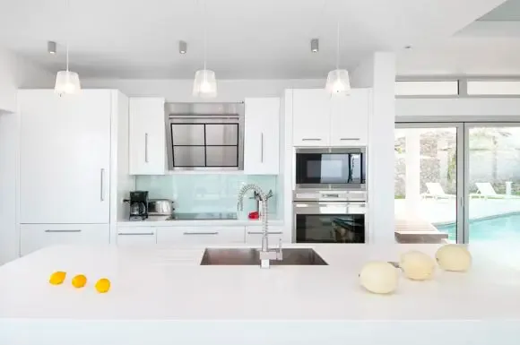 Contemporary kitchen with integrated sink and fresh fruit display, double oven, stainless steel range hood, and glass doors opening to the pool terrace.                                                                                                                                                                                                                                                                                                                                                                 +
 