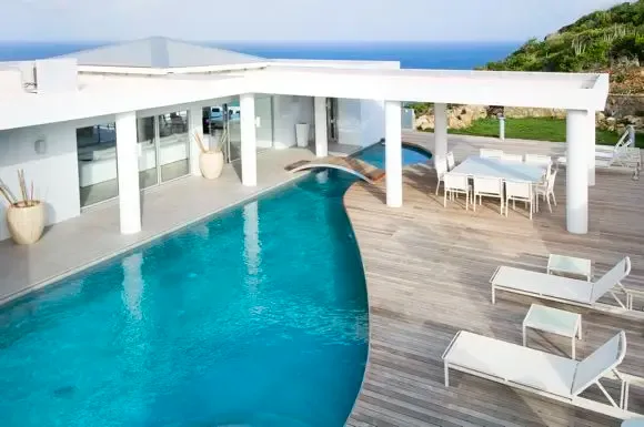A curved swimming pool features a charming wooden bridge, while the spacious deck offers lounge chairs, outdoor dining pavilion, and breathtaking ocean views.                                                                                                                                                                                                                                                                                                                                                              +
 