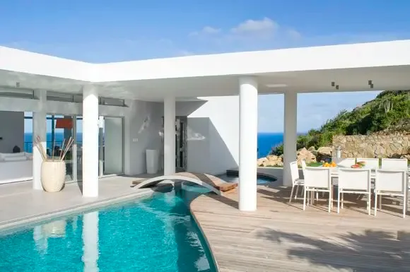 An L-shaped swimming pool with arched wooden bridge anchors the terrace, where shaded outdoor dining meets stunning ocean and hillside panoramas.                                                                                                                                                                                                                                                                                                                                                                           +
 