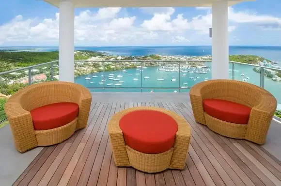 Circular woven wicker lounges with red cushions create an intimate conversation area overlooking the turquoise harbor dotted with sailboats.                                                                                                                                                                                                                                                                                                                                                                             +
 