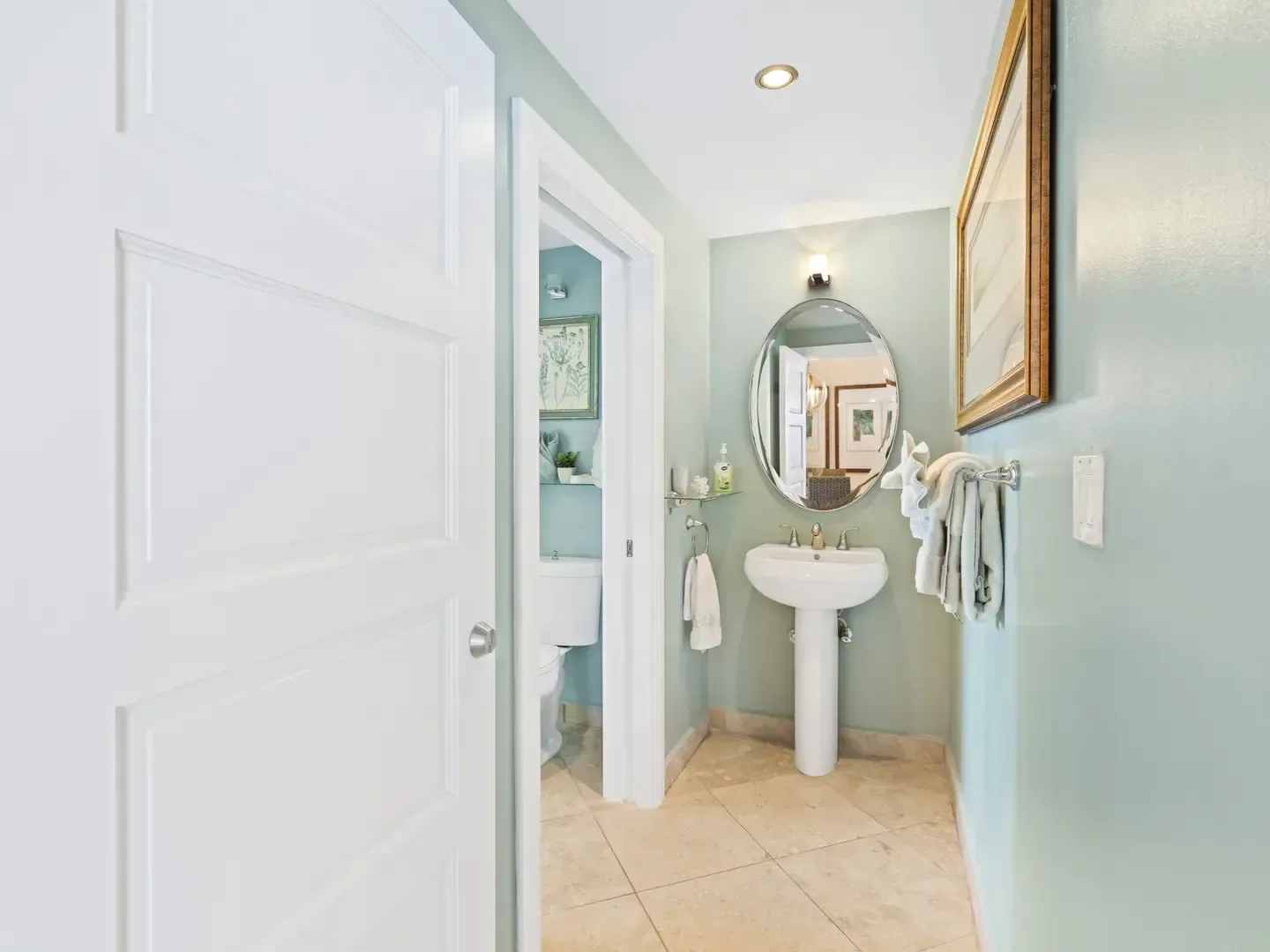 Bathroom with mint green walls, white pedestal sink, oval mirror, and beige tile flooring