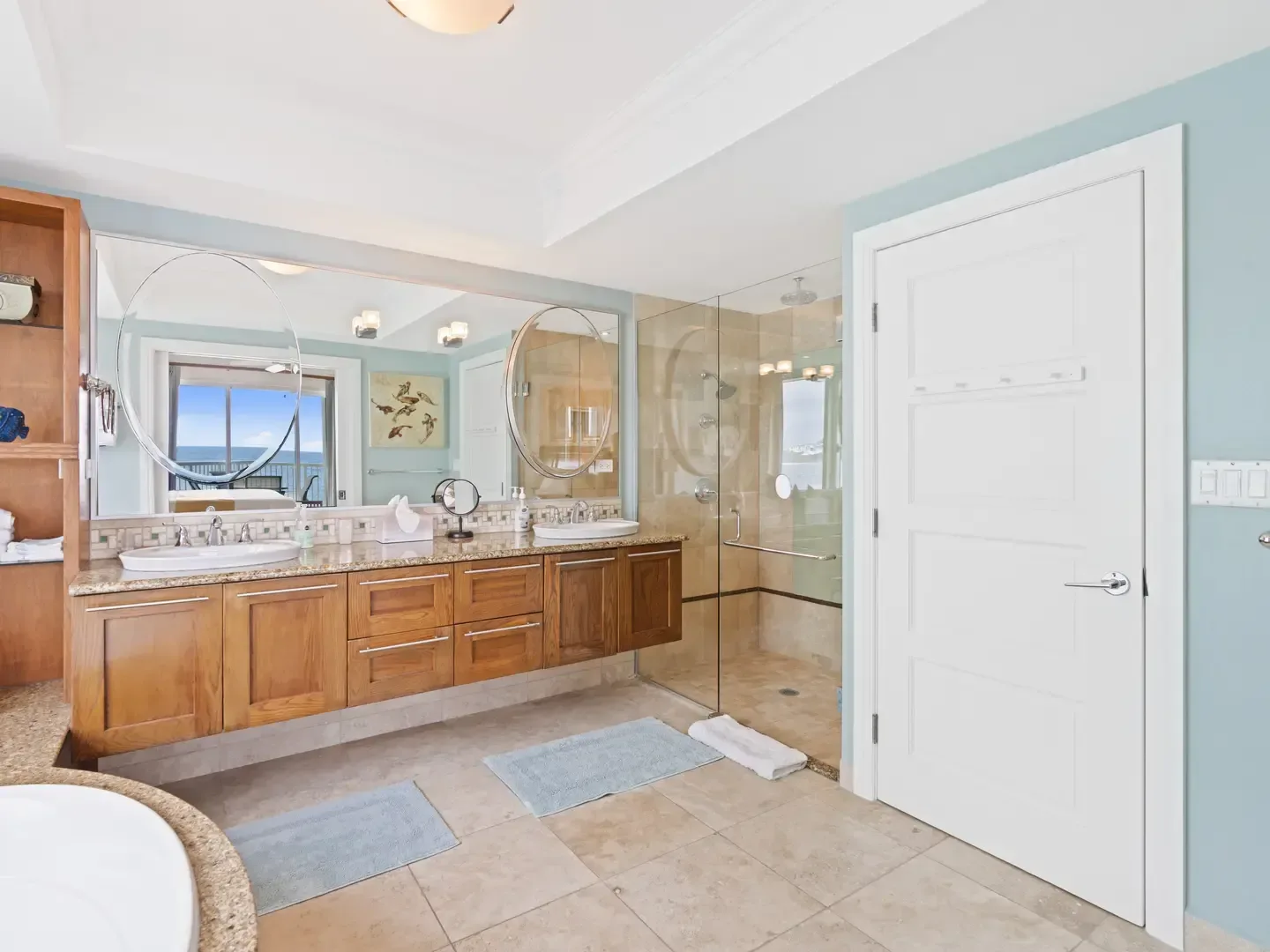 Luxurious villa bathroom with ocean view, double sinks, glass shower, blue walls, and wooden cabinetry