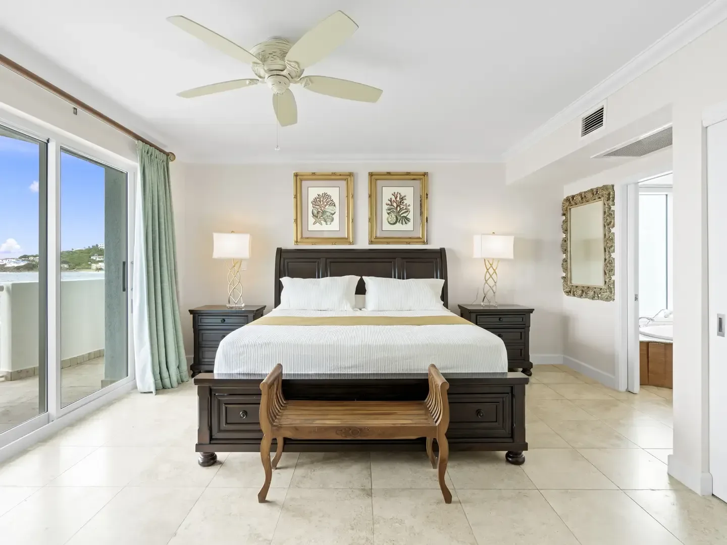 Spacious bedroom with king bed, ocean view through sliding glass doors, coral artwork, and green curtains