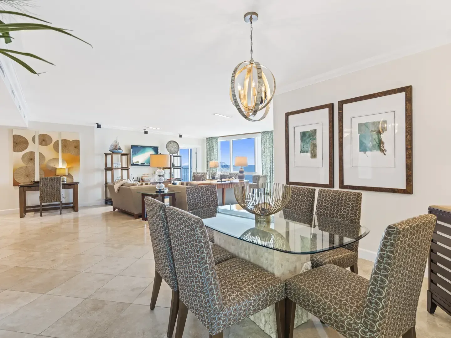 Spacious open-concept villa interior with glass dining table, patterned chairs, living room, and ocean view through large windows