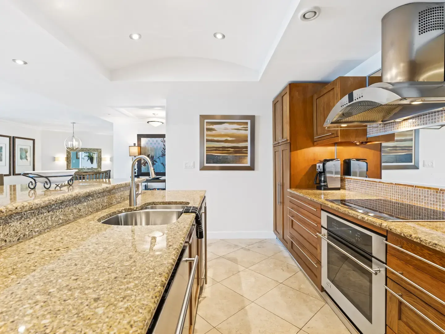 Modern kitchen with granite countertops, stainless steel appliances, wooden cabinets, and dining area with ocean-themed artwork
