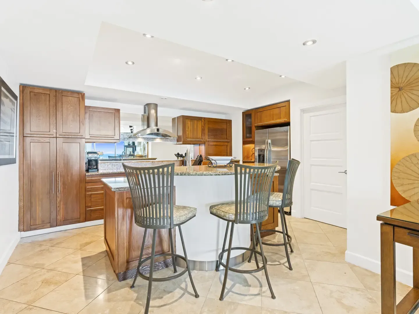 Modern kitchen with wooden cabinets, central island, bar stools, and ocean view through window
