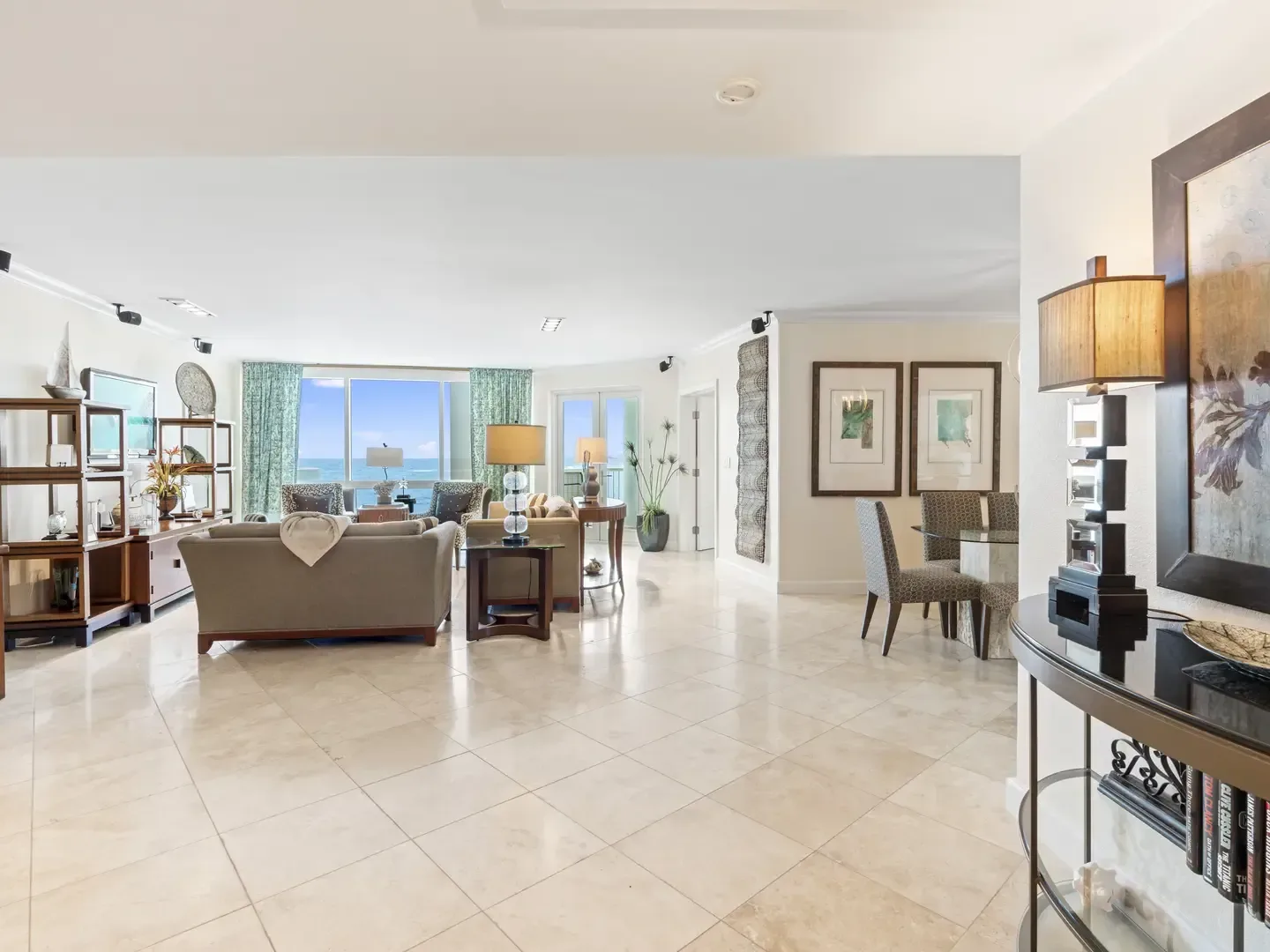 Spacious open-concept living and dining area with ocean view, beige sofas, glass dining table, and marble flooring