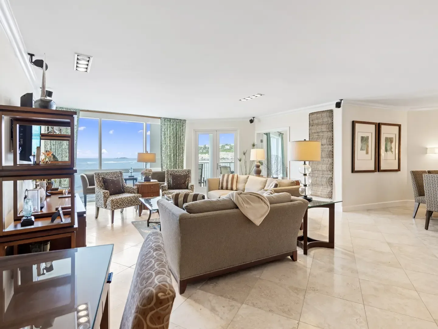 Spacious villa living room with ocean view, beige sofas, leopard-print armchairs, glass tables, and large windows overlooking the blue sea