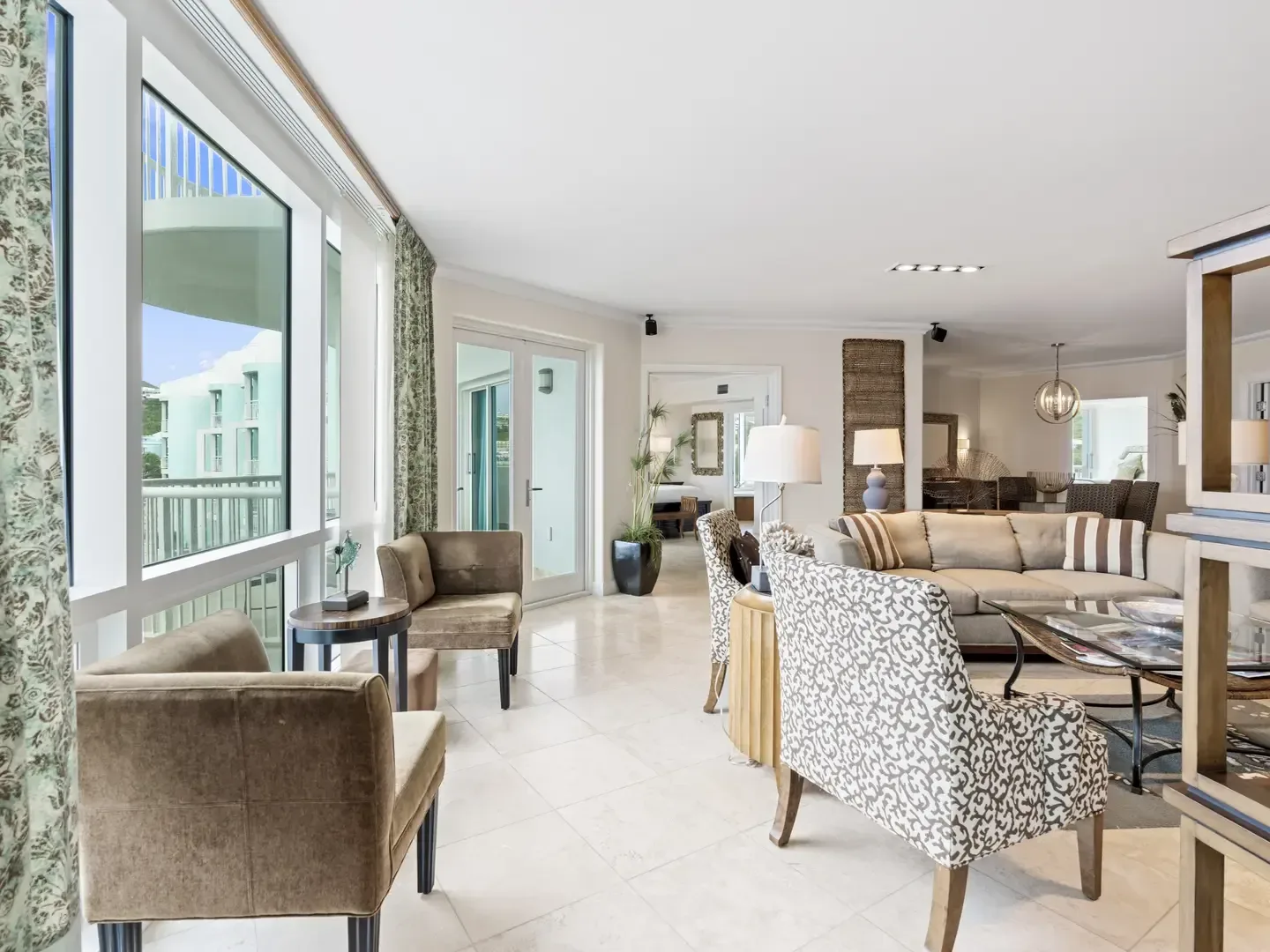 Spacious villa living room with neutral furniture, large windows, and outdoor view of turquoise building