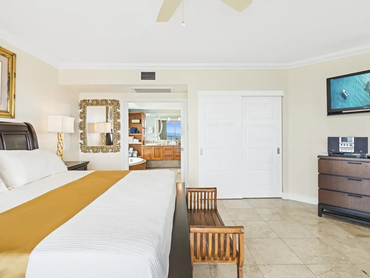 Spacious master bedroom with king bed, ocean view from bathroom, wooden furniture, and flat-screen TV